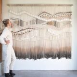 Großes gewebtes Wandkunstwerk in Creme- und Grautönen neben einer Person