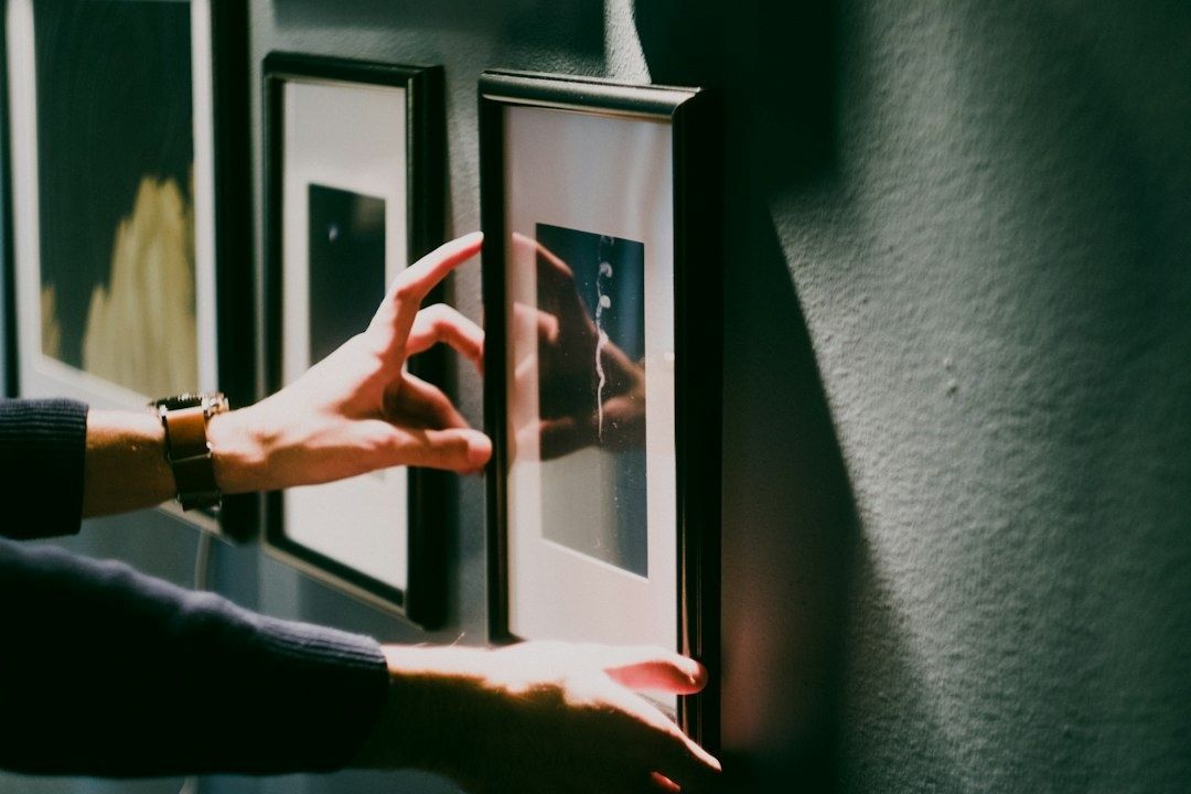 Hände richten einen gerahmten Druck an einer Wand aus